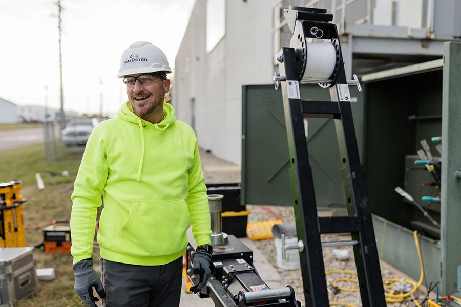 electrician using a wire pulling machine outdoors with PPE and organized jobsite setup demonstrating construction safety management practices