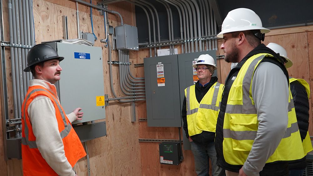 Industrial team reviewing electrical control panels and conduit layout inside facility