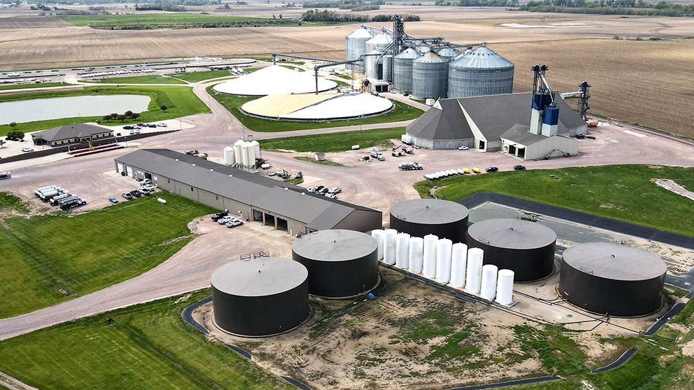 Aerial view of agricultural processing facility with grain bins, liquid storage tanks and surrounding farmland