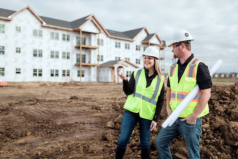Electrical contractors reviewing plans on a multifamily jobsite while wearing required safety gear